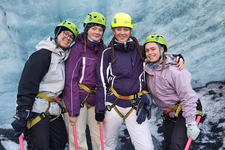 Four smiling women in helmets and harnesses posing on Sólheimajökull glacier during a guided walk