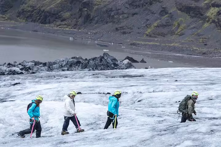Four hikers with yellow helmets and ice axes walking across Sólheimajökull glacier in Iceland