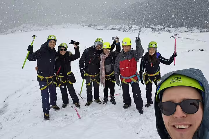 Group of hikers in yellow helmets and harnesses posing with ice axes on Sólheimajökull glacier in snow