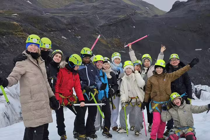 Group of tourists in yellow helmets with ice axes posing on Sólheimajökull glacier, Iceland