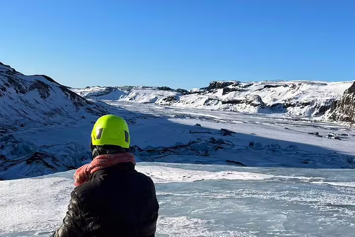 Hiker in yellow helmet overlooking Sólheimajökull glacier and snow-covered landscape in Iceland