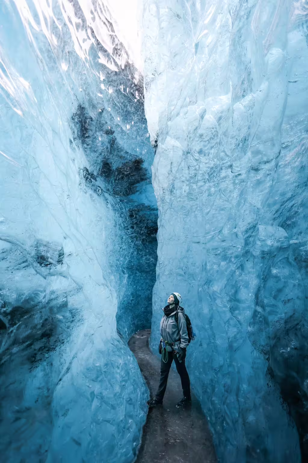Solo explorer in helmet stands inside a narrow blue glacier ice cave during a private photoshoot adventure