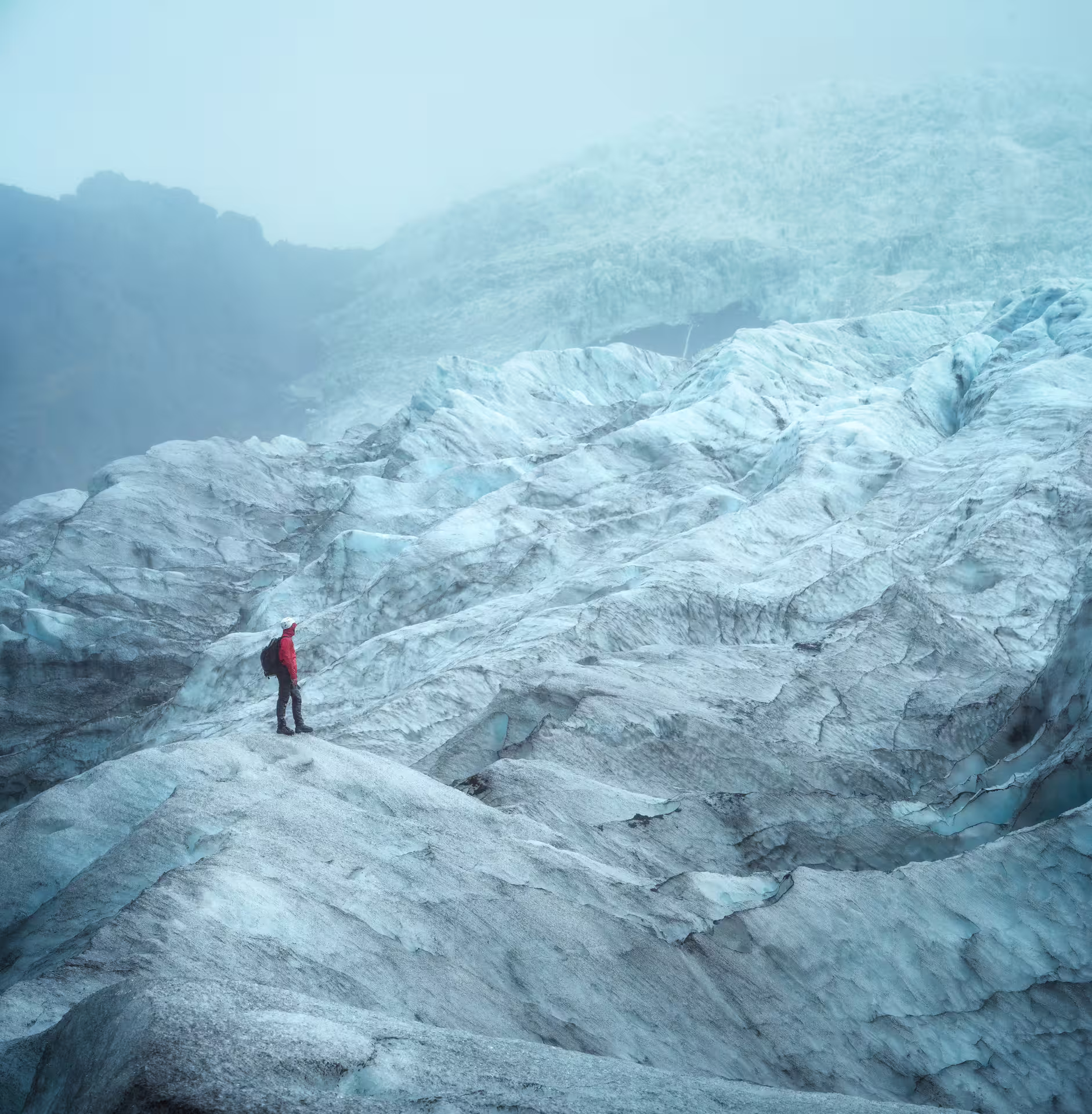 Solo hiker in red jacket standing on vast textured glacier surface during private early bird ice cave adventure tour