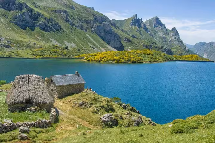 Scenic view of Somiedo Natural Park with a serene lake, mountains, and rustic cottages, perfect for guided tours from Oviedo.