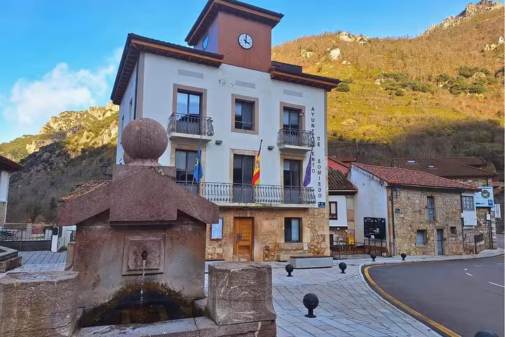 Charming village building with flags and a stone fountain in Somiedo, Asturias, showcasing local architecture and culture.