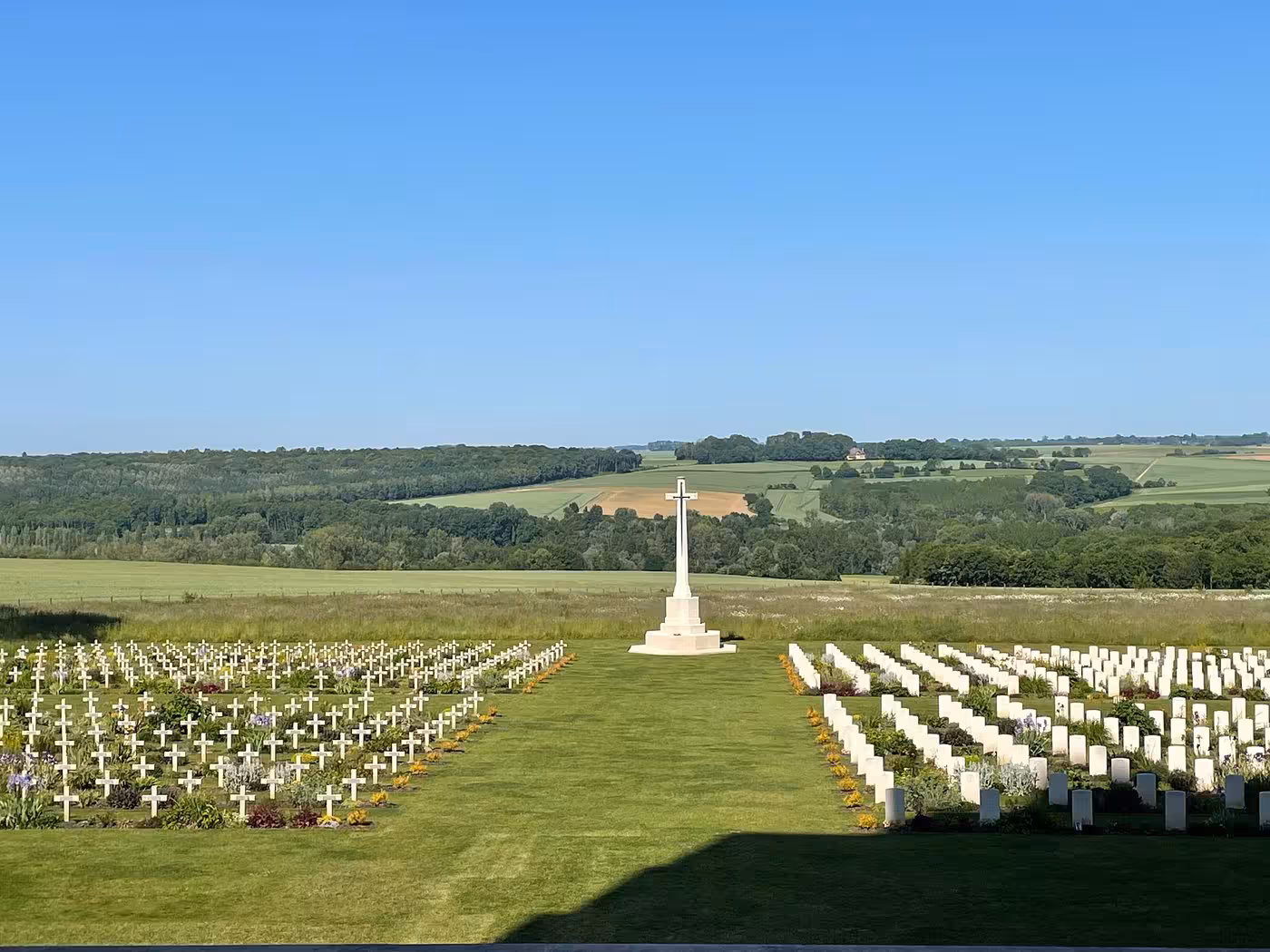 Rows of white war graves and cross monument at Somme Battlefield cemetery, France, with rolling green countryside