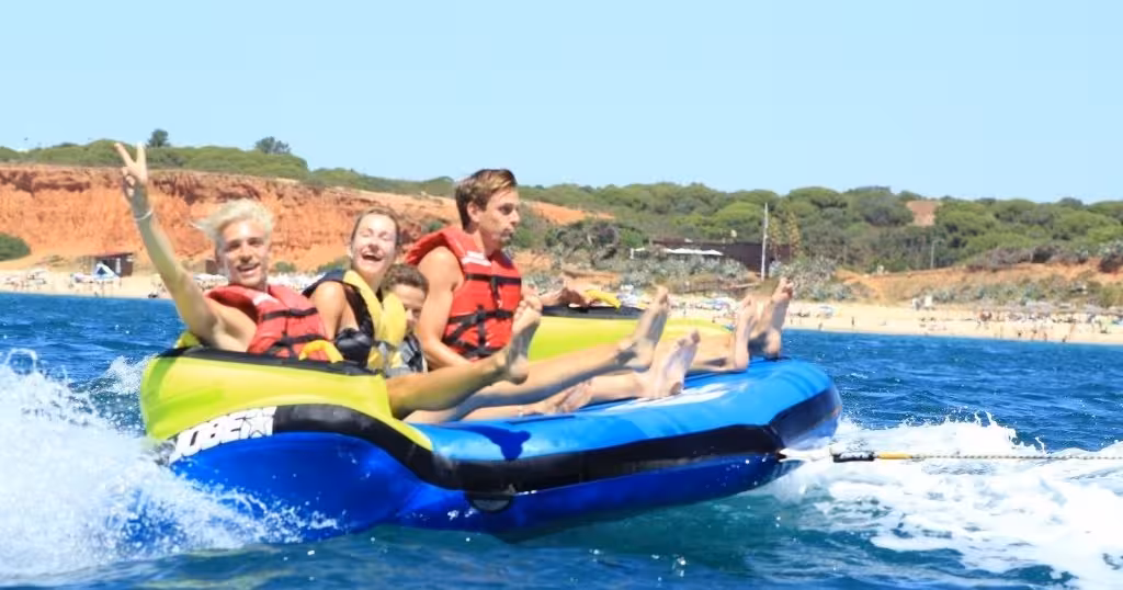 Group of friends on Sonar inflatable sofa being towed over blue waves near Algarve beach cliffs on a summer adventure tour