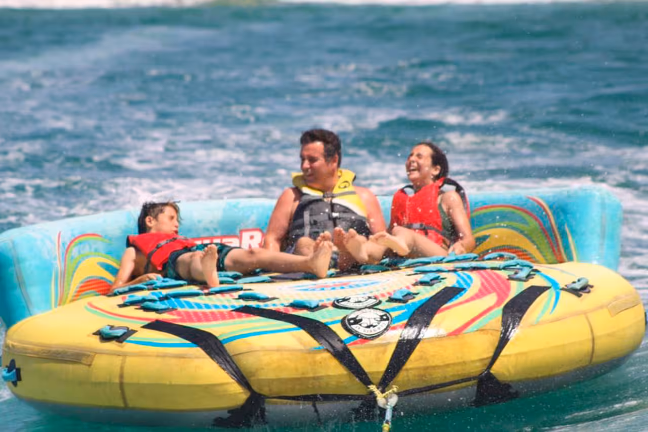 Family laughing together on Sonar inflatable tube ride, skimming across turquoise ocean on a safe, fun water activity