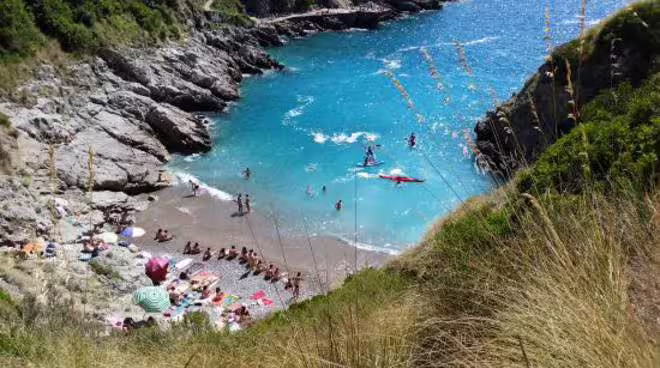 Hidden cove near Ieranto Bay with swimmers and kayaks in turquoise water on Sorrento Amalfi Coast boat tour experience