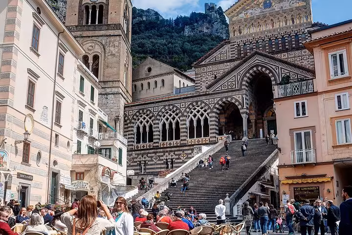 Vibrant scene at Amalfi's Piazza del Duomo with tourists enjoying cafes and the stunning cathedral backdrop.