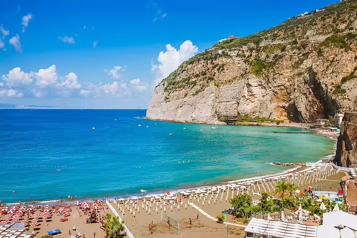Panoramic view of Sorrento beach cove with turquoise water, sunbeds, and cliffside on Naples day tour