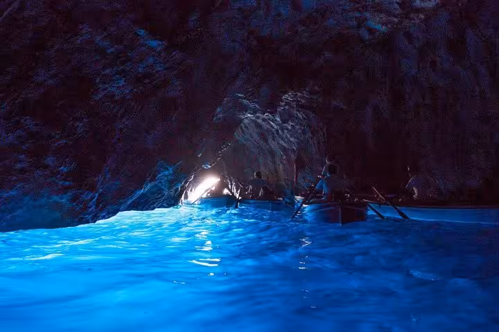 Inside the Blue Grotto, vibrant blue waters illuminate a boat tour on the Sorrento to Capri route.