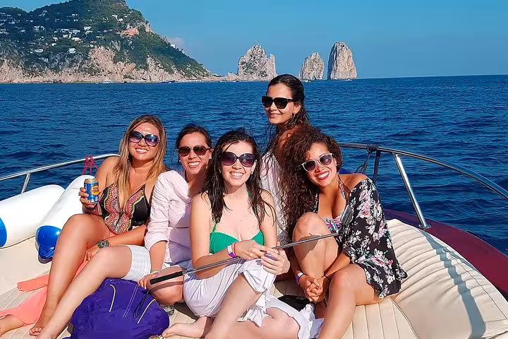 Group of friends relaxing on a classic Gozzo 7.50 boat with Capri's iconic Faraglioni rocks in the background.