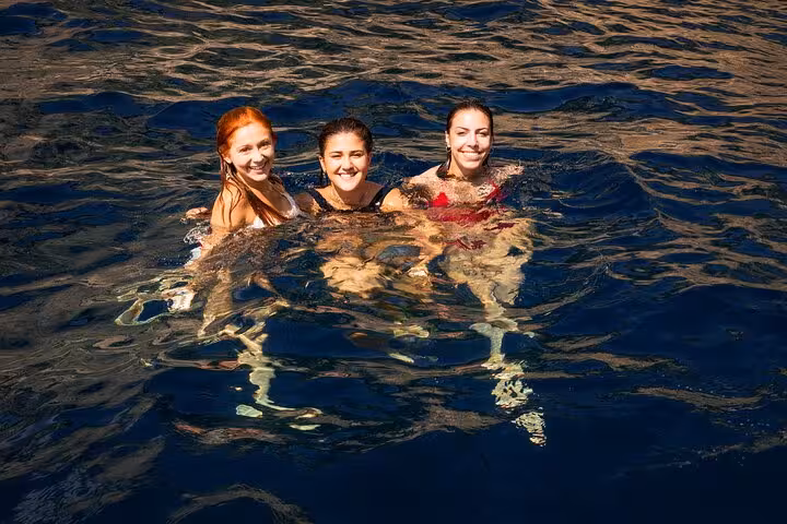 Three smiling women swimming in the clear blue waters of the Sorrento Coast during a small group boat tour.