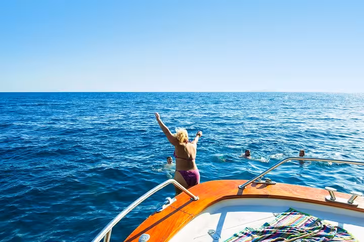 Person leaps into the vibrant blue waters from a boat during a Sorrento Coast small group tour, showcasing adventure.
