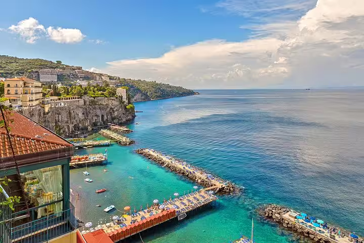 Panoramic view of Sorrento coastline with turquoise waters, cliffside buildings, and marina pier in Naples, Italy