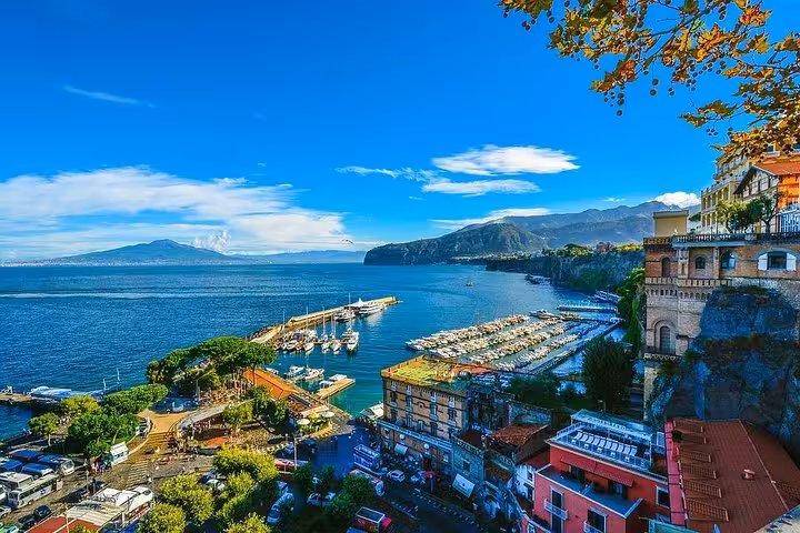 Panoramic view of Sorrento's vibrant coastline with marina and Mount Vesuvius in the background, perfect for scenic travel experiences.