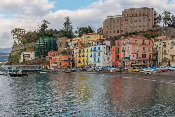Colorful waterfront buildings and boats along the sandy shore of Sorrento, Italy