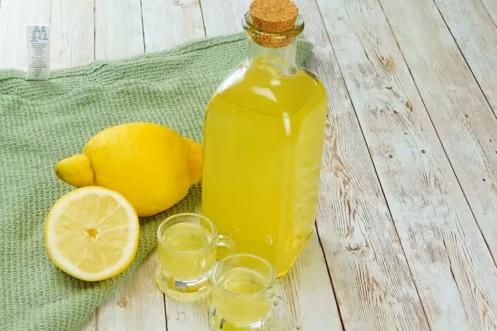 Refreshing limoncello bottle with fresh lemons on rustic wooden table, highlighting Sorrento's famous citrus flavors.
