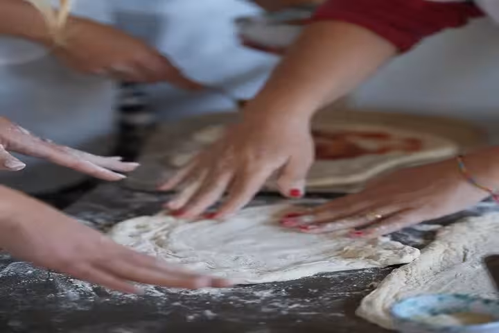 Hands kneading pizza dough, highlighting the interactive process of a farm-to-table culinary experience.