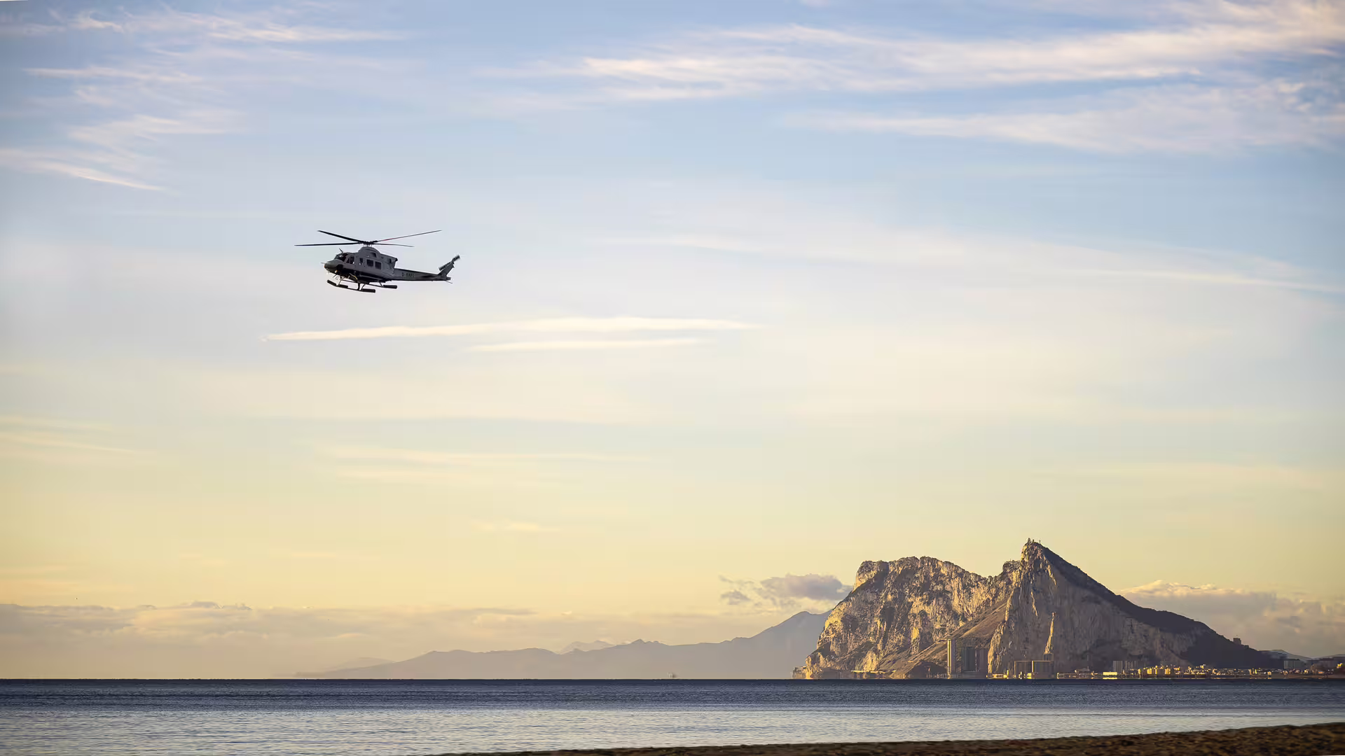 A helicopter flies over the serene coastline with the Rock of Gibraltar in view, seen from a Sotogrande boat charter.