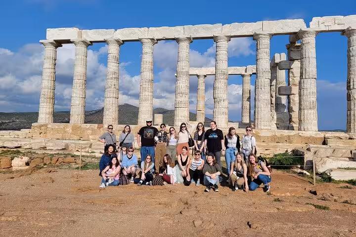 Tour group posing in front of the iconic Temple of Poseidon at Cape Sounio during a sunny day.