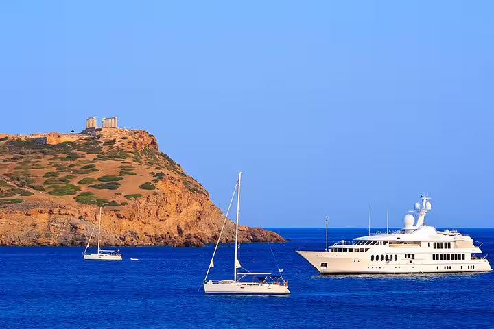 Yacht and sailboats near Cape Sounion with Temple of Poseidon on the headland, Athens Riviera sunset tour