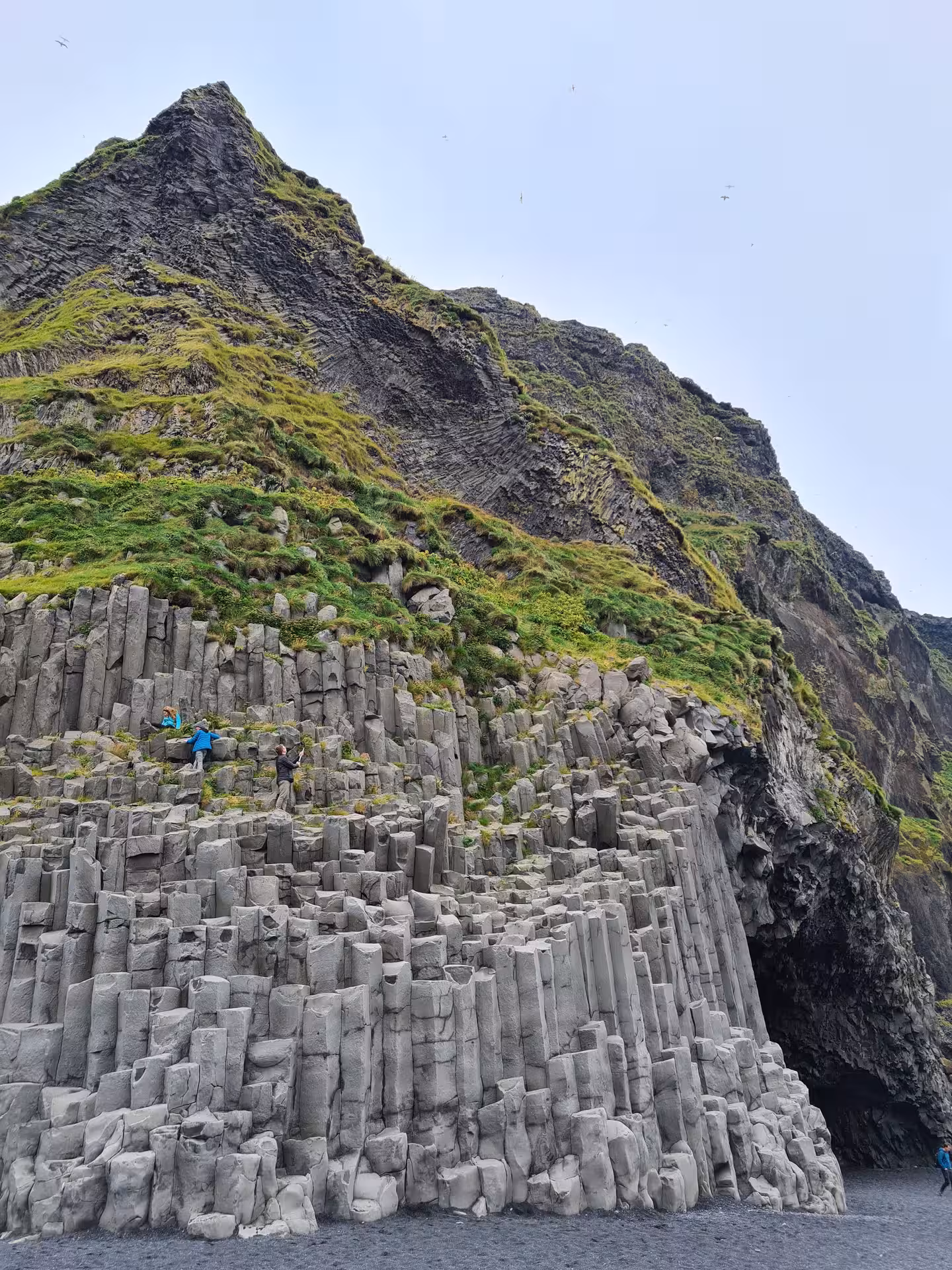 Basalt column sea cave at Reynisfjara black sand beach on Iceland's south coast with tourists climbing