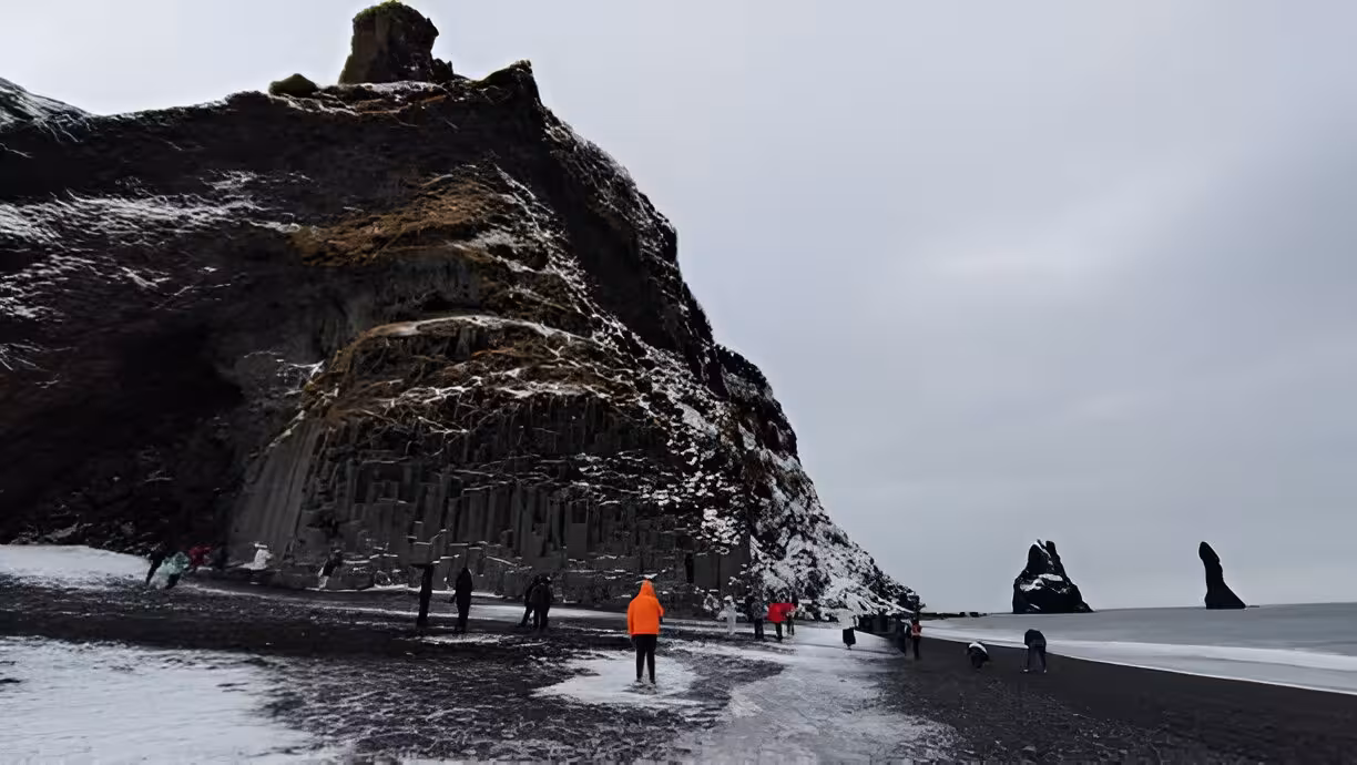 Tourists exploring Reynisfjara black sand beach with basalt columns and sea stacks in Iceland