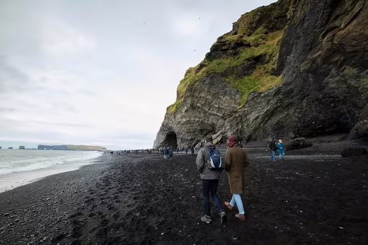Tourists walking on Reynisfjara black sand beach along dramatic cliffs on Iceland's South Coast