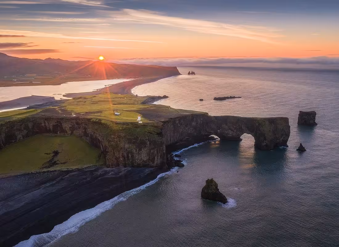 Aerial sunset view of Dyrhólaey rock arch and black sand beach on Iceland's South Coast