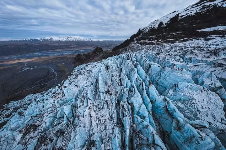 Blue glacial ice formations on Iceland's South Coast glacier with snow-capped mountains in the background
