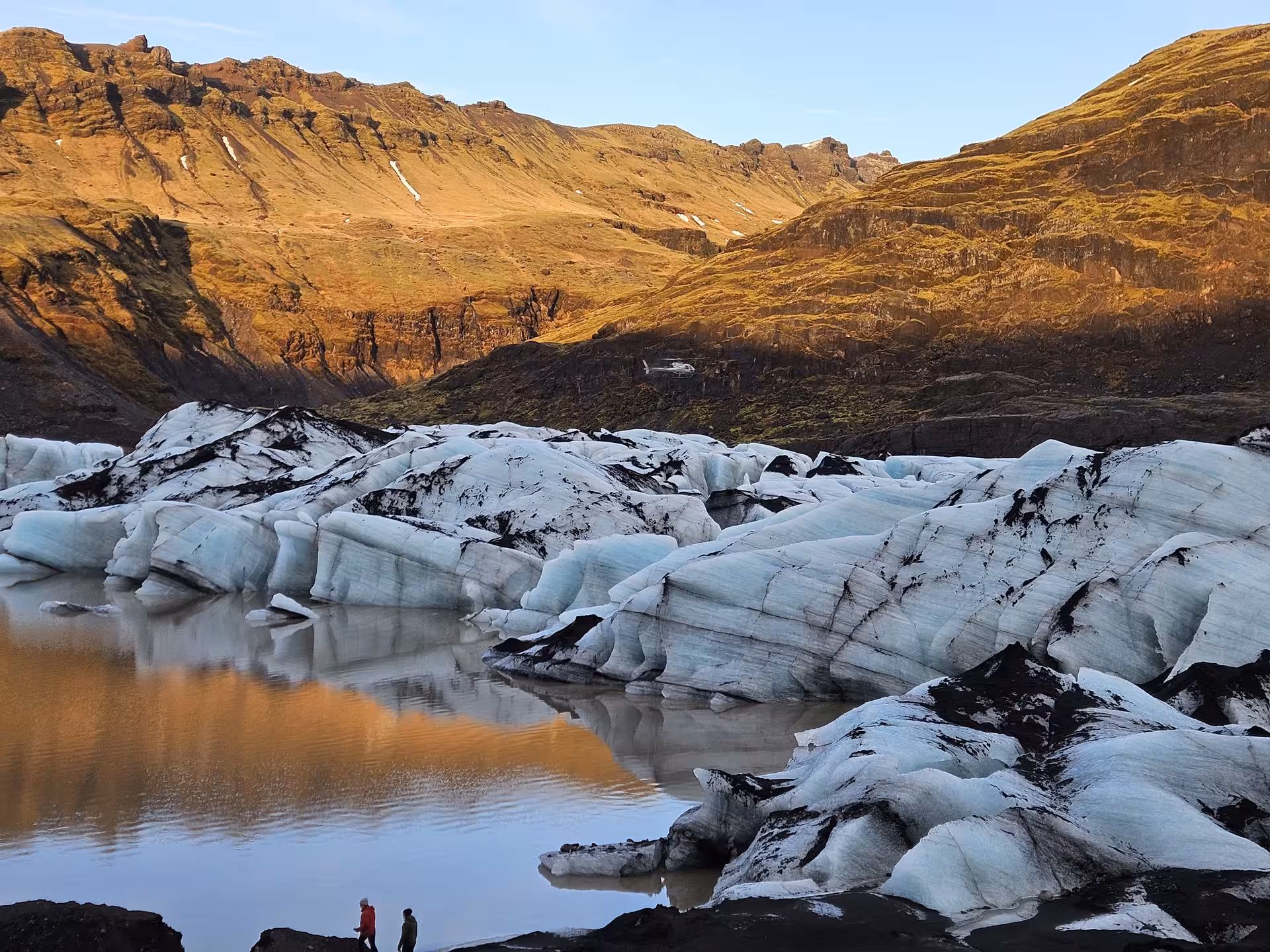 Family guides standing beside glacier ice formations and glacial lagoon with mountain backdrop in South Iceland
