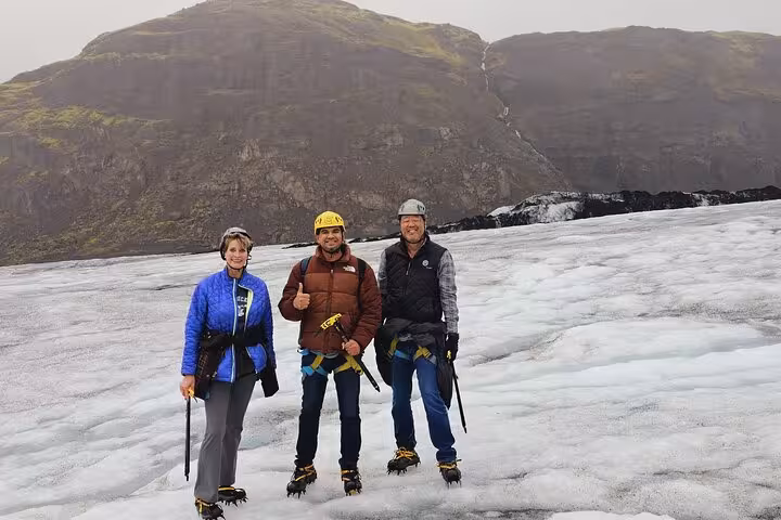 Three hikers with crampons and ice axes posing on a glacier with mountain backdrop in Iceland