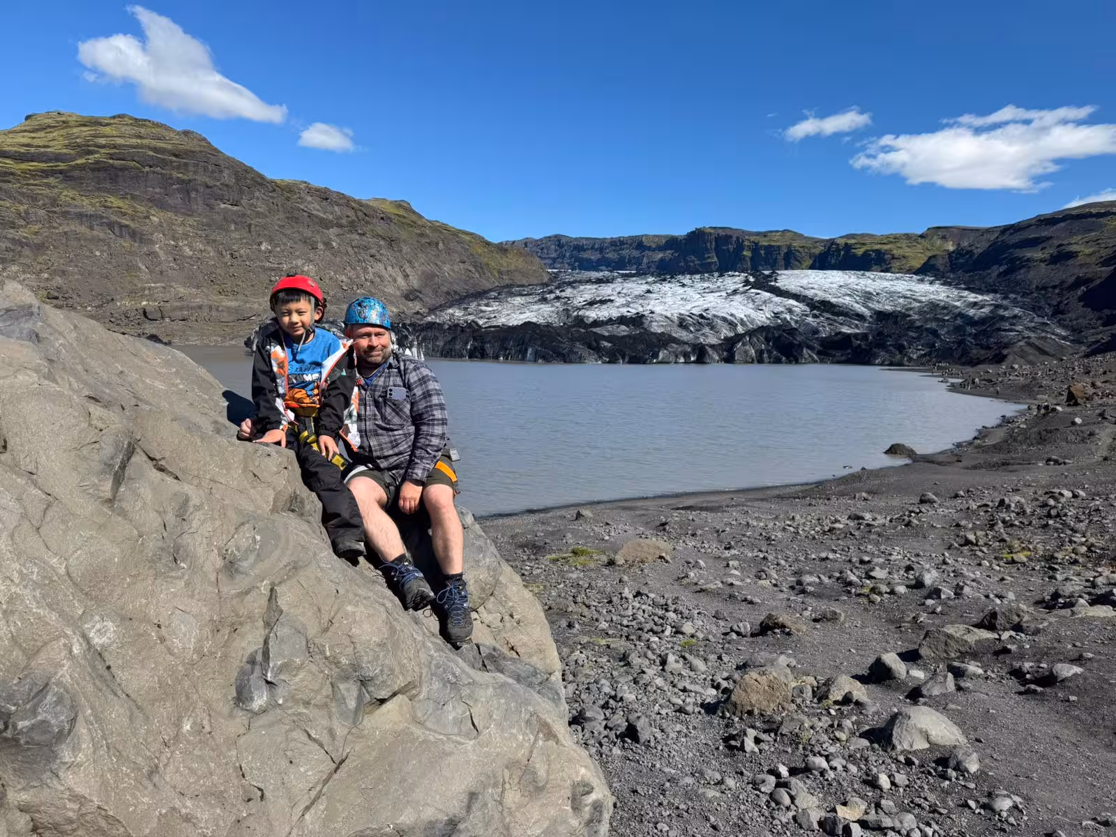 Father and child sitting on rock at Sólheimajökull glacier lagoon on Iceland's South Coast