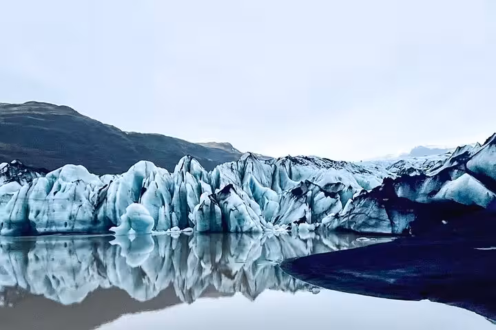 Glacial ice formations reflected in calm dark waters with mountain backdrop on Iceland's south coast