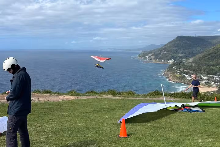 Hang glider soaring over scenic South Coast cliffs, perfect for adventure seekers on a private tour.