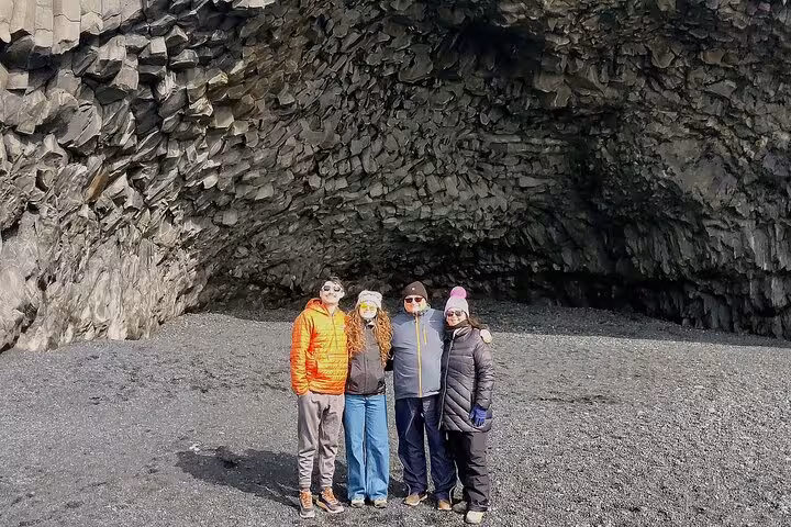 Four tourists posing at Reynisfjara black sand beach cave on Iceland South Coast tour