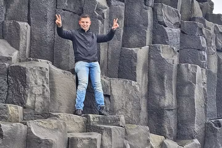 Tourist posing with peace signs on black basalt rock columns on Iceland's South Coast