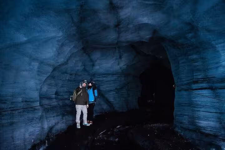 Two tourists exploring a blue ice cave on Iceland's South Coast glacier tour