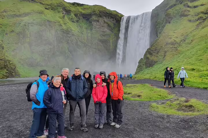 Tour group posing in front of Skógafoss waterfall on Iceland's south coast on a cloudy day