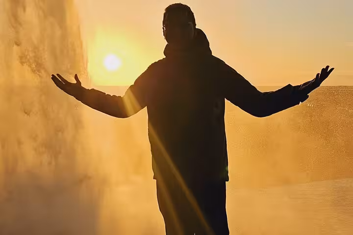 Silhouette of a person with arms outstretched near a waterfall at golden sunset in Iceland