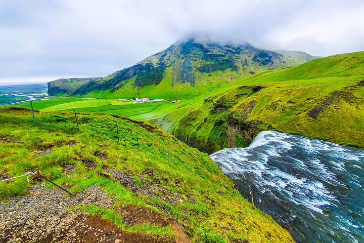 Sweeping green South Coast Iceland landscape with river and misty mountain views from Reykjavik tour