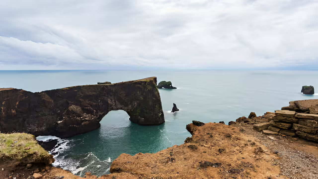 Natural rock arch over turquoise waters on Iceland's south coast with sea stacks in the background