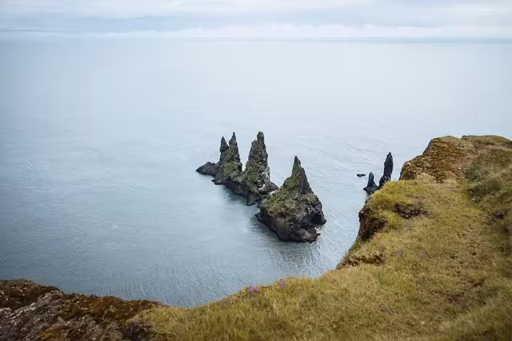 Dramatic black rock sea stacks rising from calm ocean along Iceland's south coast cliffs