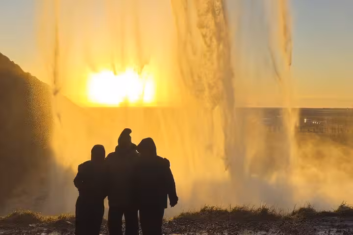 Silhouettes of tourists watching Seljalandsfoss waterfall at golden sunset on Iceland South Coast tour