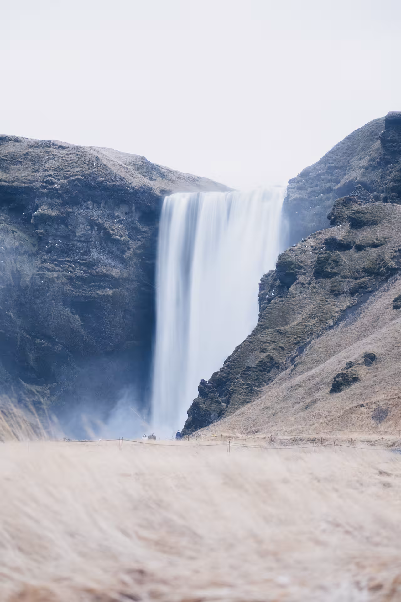Skógafoss waterfall cascading down cliffs with golden grasslands in Iceland's South Coast