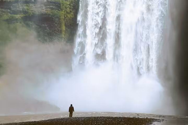 Person standing before massive waterfall on Iceland's south coast tour