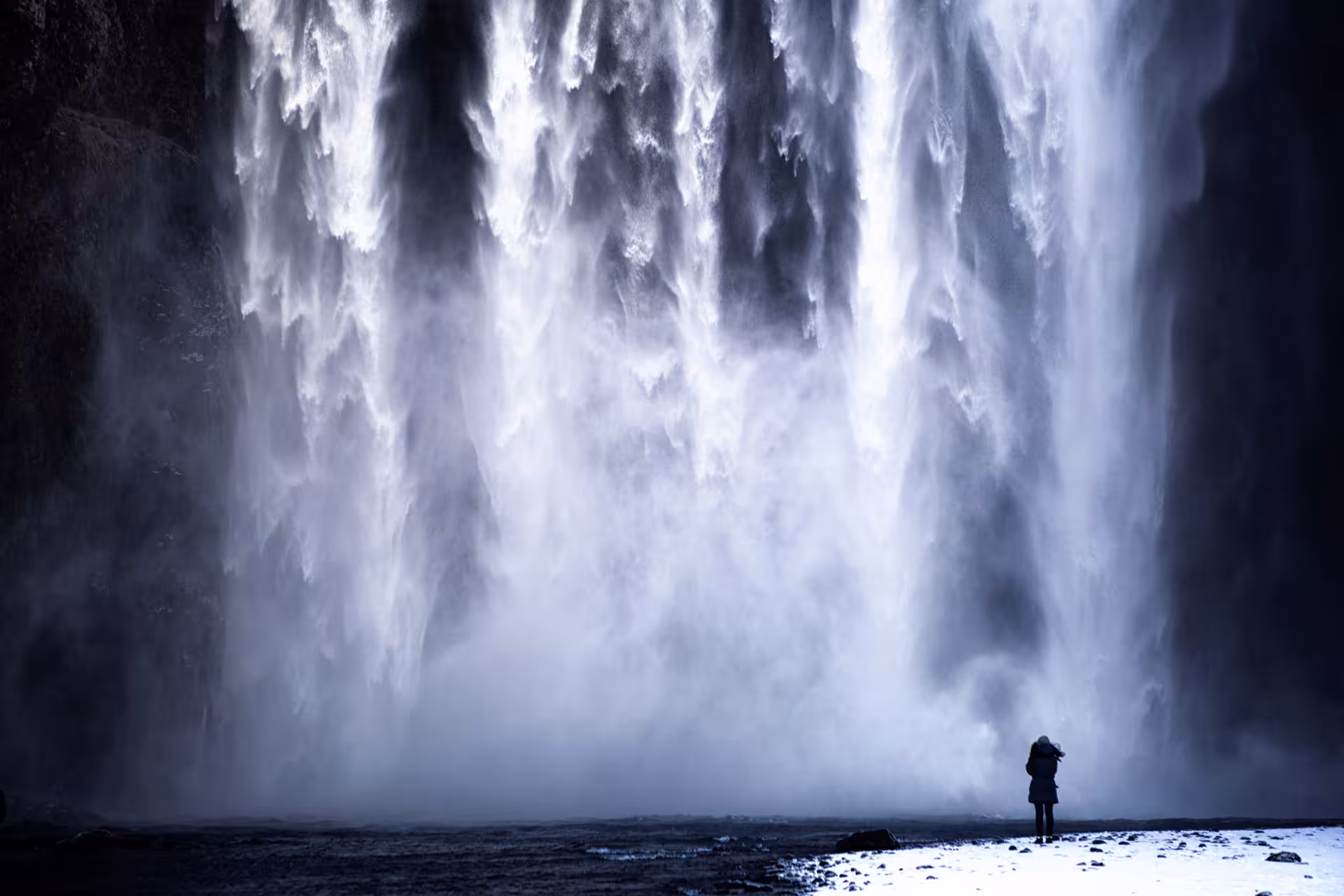 Lone traveler standing before massive Skógafoss waterfall mist on Iceland's South Coast