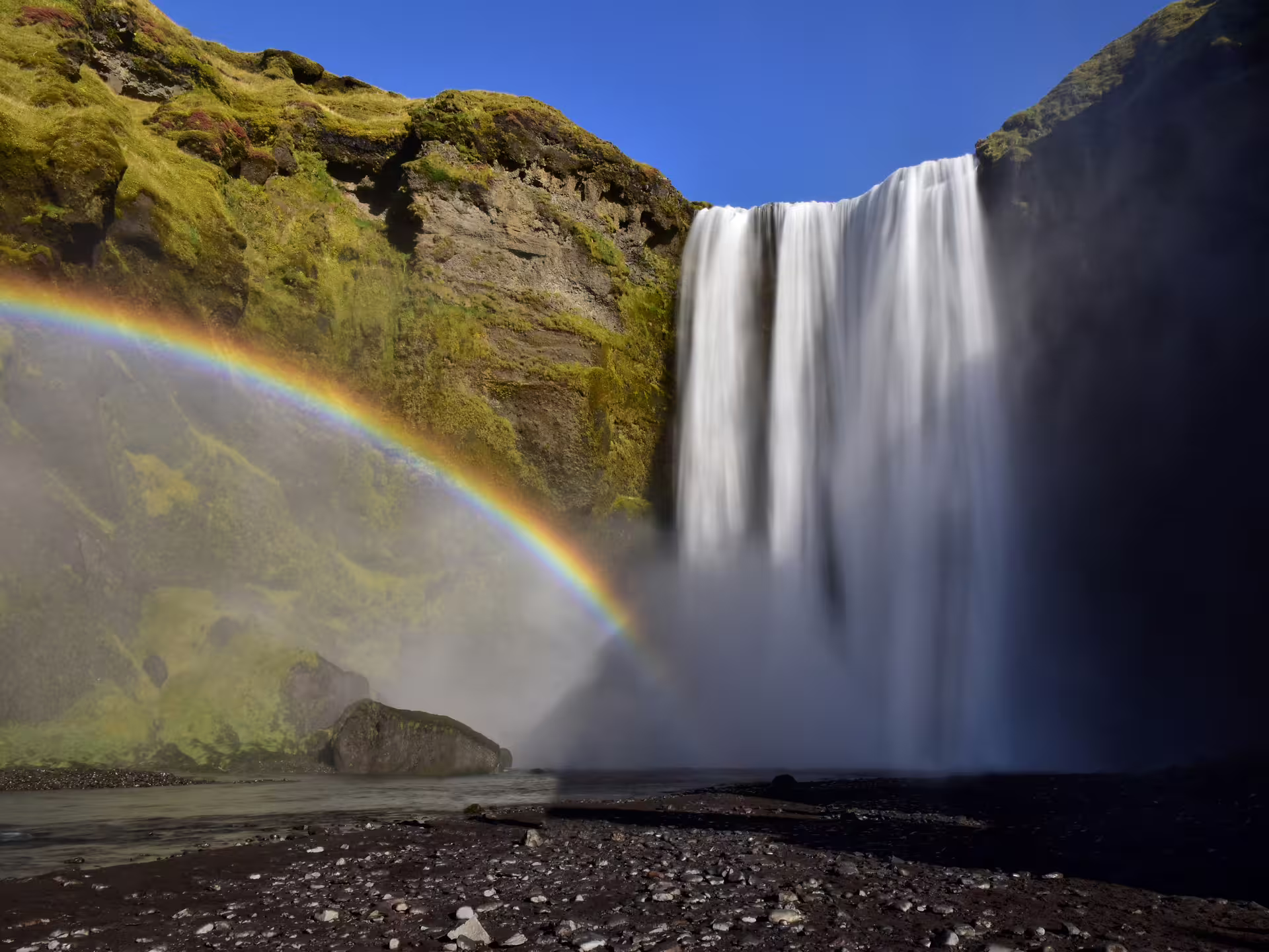 Skógafoss waterfall with double rainbow and moss-covered cliffs on Iceland's south coast